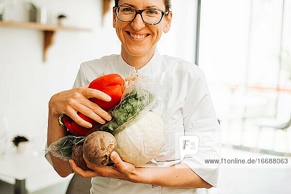 Weibliche Köchin lächelt in die Kamera und hält frisches Gemüse