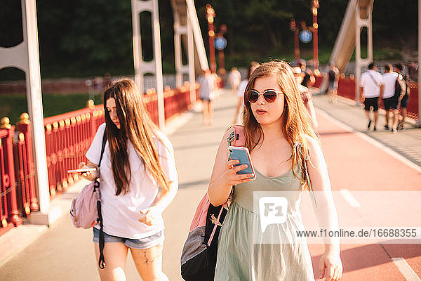 Zwei junge Frauen mit Smartphones auf einer Brücke im Sommer