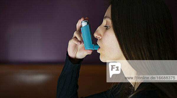 Frau  die zu Hause einen blauen Asthma-Inhalator inhaliert.