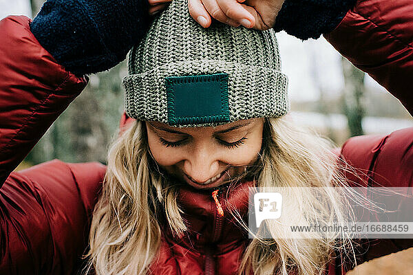 Frau hält fröhlich ihren Hut in einem windigen Wald in Schweden