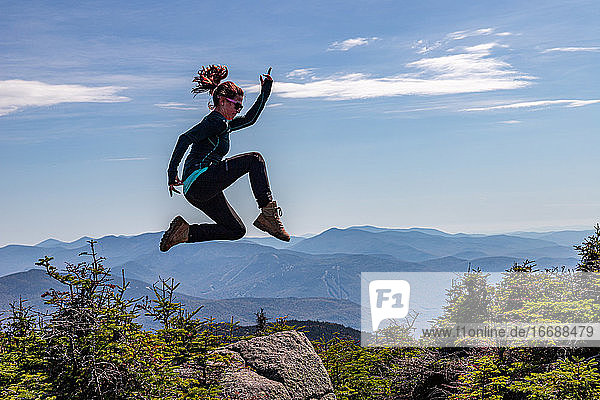Junge sportliche Frau  die auf dem Gipfel eines Berges in Pose springt.