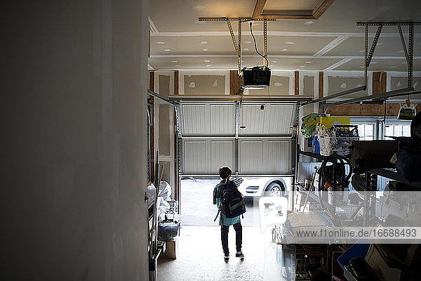 Teenager-Junge mit Rucksack geht aus einer unordentlichen Garage  während sich die Tür öffnet