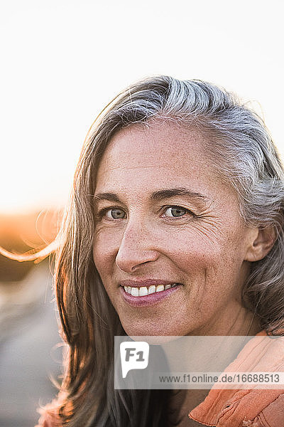Porträt einer grauhaarigen Frau am Strand bei Sonnenuntergang