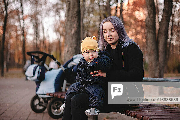 Glückliche junge Mutter mit ihrem kleinen Sohn auf einer Bank im Park sitzend