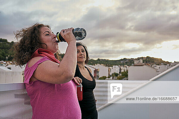 Zwei Frauen mit echten Körpern trinken Wasser aus ihren wiederverwendbaren Flaschen