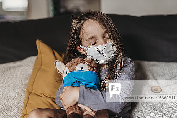 Preschool age girl with mask on cuddling stuffed animal with mask
