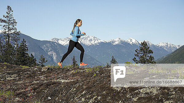 Seitenansicht einer starken Sportlerin  die beim Fitnesstraining auf dem Lande gegen einen verschneiten Bergkamm läuft