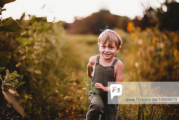 Fröhlicher Junge in grüner Latzhose  der durch ein Blumenfeld läuft