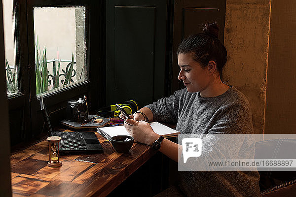 Junge Frau schaut auf ihr Handy  während sie in einer Retro-Kneipe lernt