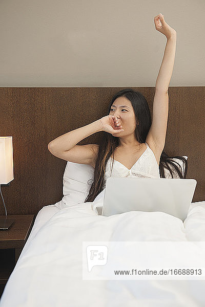 schöne Frau wacht auf und überprüft ihren Laptop im Hotelzimmer