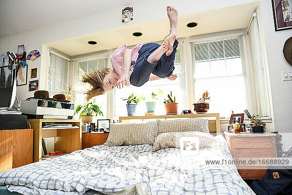 Teenager  der auf dem Bett springt  in der Luft gefangen wird und im sonnigen Schlafzimmer lächelt