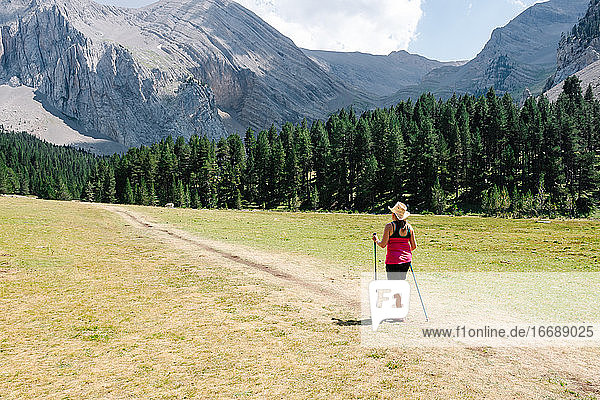 hiker woman wearing straw hat  shorts and backpack on the path across a plain walking with amazing mountains at the background while enjoys the natural environment around. Horizontal photo.