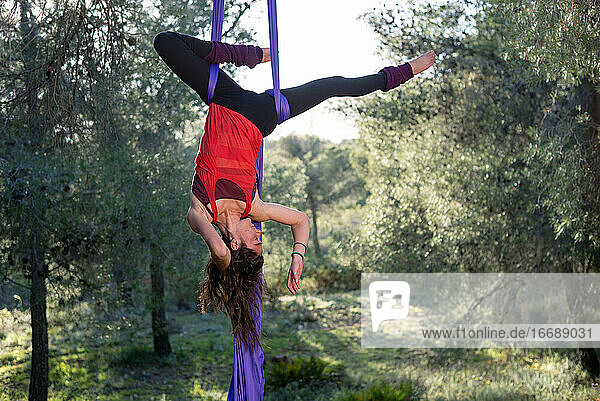 Junges Mädchen  Akrobatin. Übt Seiltanz in der Luft. Frau macht Zirkuskunststücke mit Kleidung im Wald. Umgekehrte Hüftblockposition.