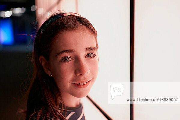 portrait of a smiling girl looking into a camera next to an illuminated wall