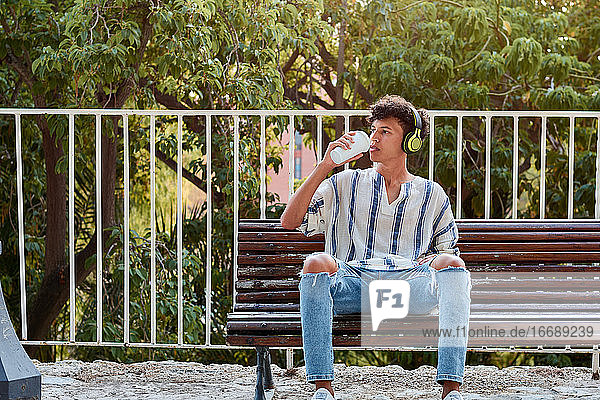 Junger Junge mit Afro-Haar trinkt Kaffee  während er auf einer Bank sitzt