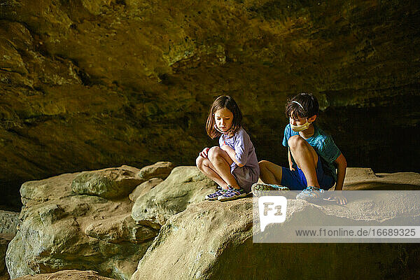 zwei kleine ernste Kinder sitzen zusammen auf einem Felsvorsprung in einer Schlucht