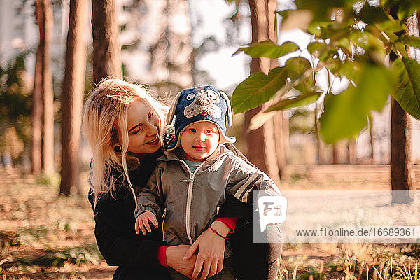Glückliche junge Mutter umarmt ihr kleines Kleinkind Sohn im Park im Herbst