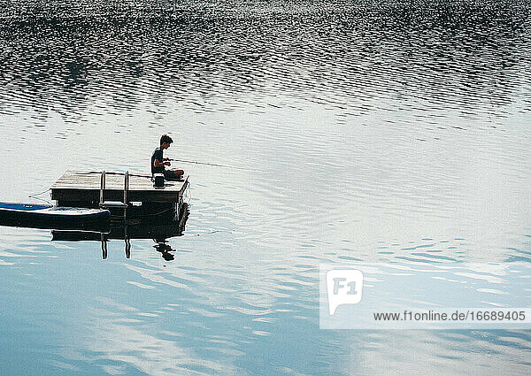 Teen boy fishing from a swim platform on a lake in the summer.