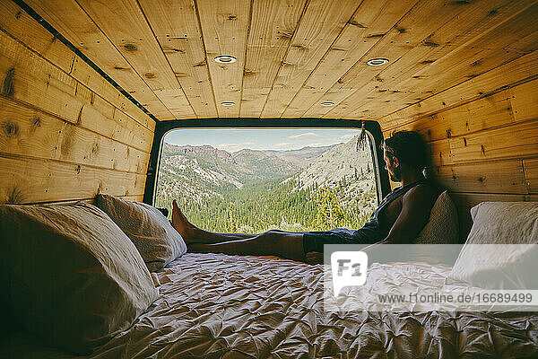 Junger Mann sitzt auf dem Bett eines Wohnmobils und betrachtet die Aussicht auf den Yosemite
