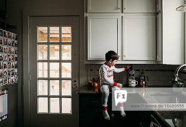 Junge sitzt auf der Küchentheke und macht Kaffee in der Morgenzeit