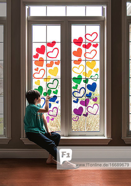Ein Junge sitzt auf der Fensterbank und ist mit einem Regenbogen aus Papierherzen bedeckt.