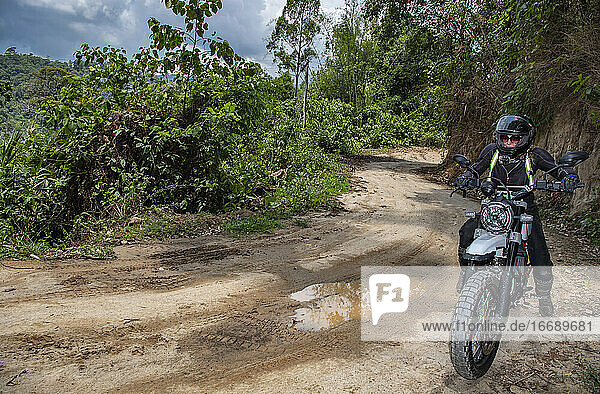 Frau fährt mit ihrem Scrambler-Motorrad auf einer schlammigen Straße in Thailand