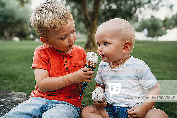 White male siblings sharing ice cream sitting on the grass