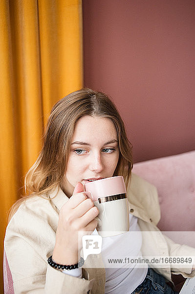 Junge Frau in Großaufnahme trinkt Tee  Kaffee in einer Keramiktasse im Wohnzimmer