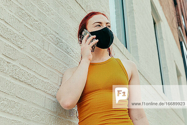 Junge Frau am Telefon mit Gesichtsmaske in einer Straße in Brooklyn.