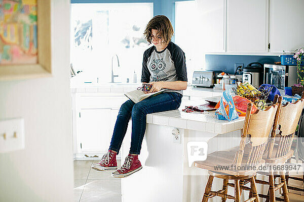Teenager-Mädchen sitzt auf dem Küchentisch und legt ihr Lesezeichen in ihr Buch