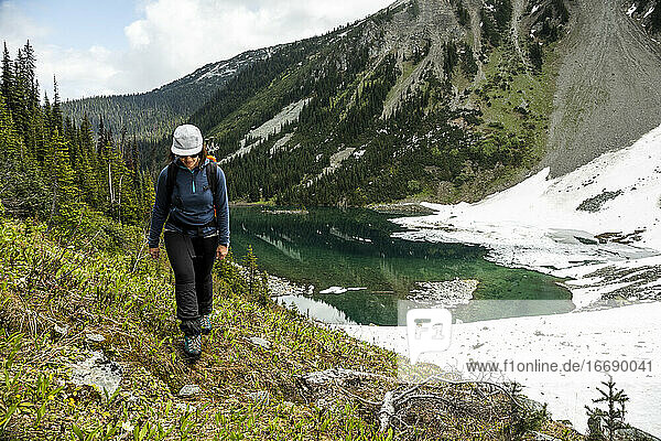Ganzkörperwanderin am Ufer eines Sees  umgeben von schneebedeckten Bergen und grünem Wald an einem Sommertag in Kanada