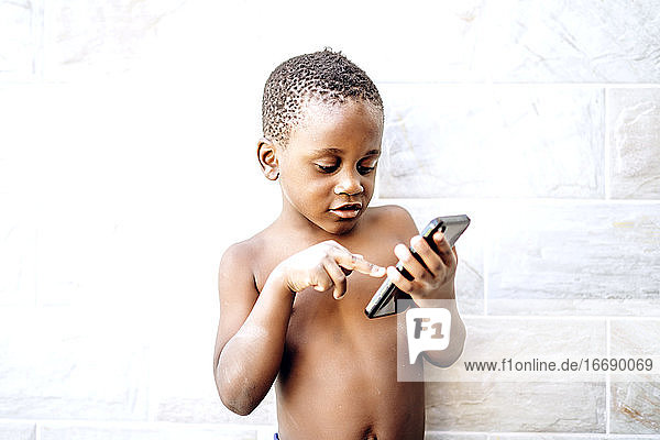 Netter afrikanischer Junge hat Spaß mit einem Mobiltelefon.