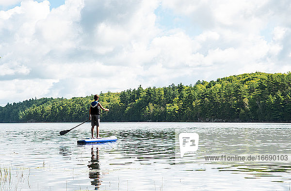 Teen boy paddling on a SUP on lake in Ontario  Canada on a sunny day.
