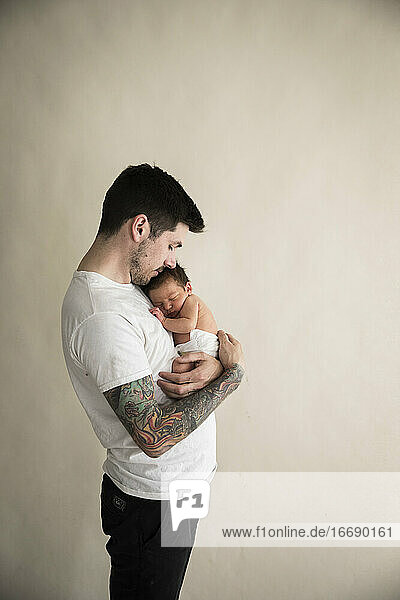 Wide Side View of Tattooed Millennial Dad Snuggling Diapered Newborn