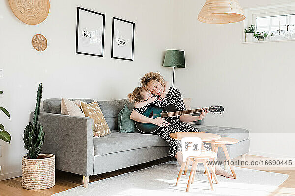 Tochter  die ihre Mutter umarmt  während sie zu Hause Gitarre spielt
