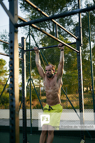Shirtless fit junger Mann trainiert in einem Käfig im Freien Fitnessstudio