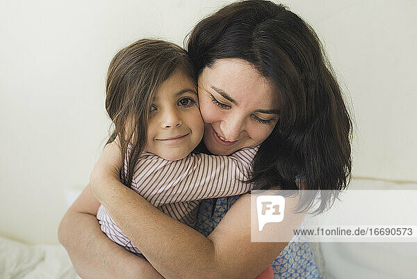 Smiling mid-30's mother hugging happy 6 yr old daughter