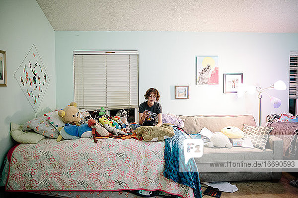 Teenager-Mädchen mit kurzen Haaren sitzt auf ihrem Bett und schaut auf ihr Handy