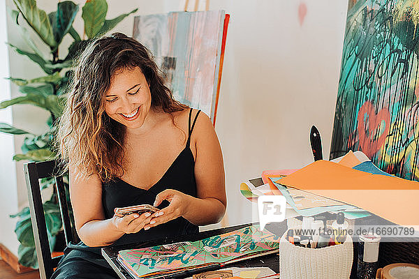 Eine Malerin benutzt ihr Smartphone  während sie im Atelier an ihren Bildern arbeitet