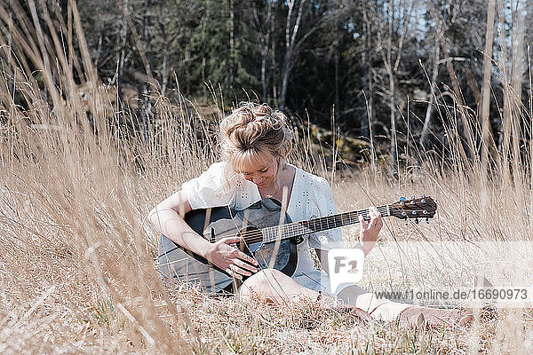 woman sat in a field happily playing guitar in summer
