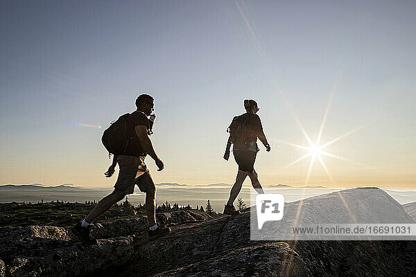 Zwei Wanderer erreichen bei Sonnenaufgang den Gipfel eines Berges in Maine