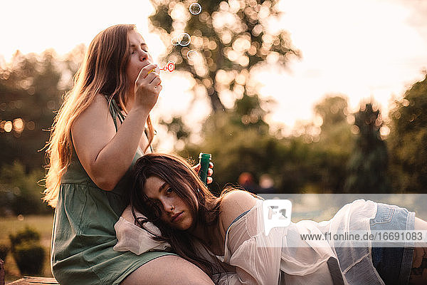 Junge Frau  die Seifenblasen bläst  während ihre Freundin auf ihrem Bein liegt