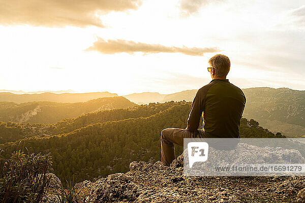Man looking the sunset sitting on a rock from the top of a mountain
