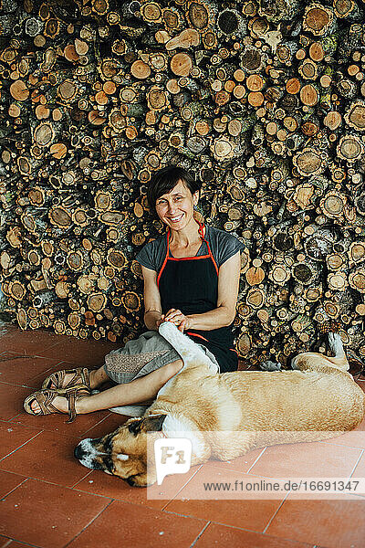 Lächelnde Frau  die mit ihrem Hund an einem Stapel Holzscheite in einem Dorf in Portugal spielt