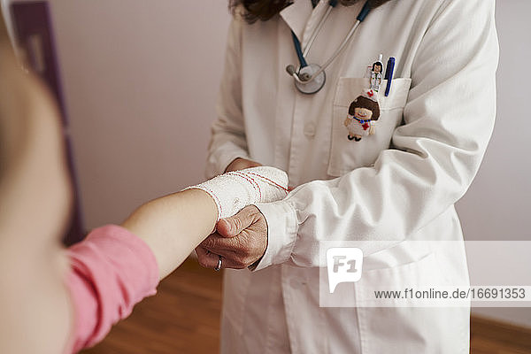 Ärztin bandagiert den Arm eines kleinen Mädchens in ihrem Zimmer. Hausarzt Konzept