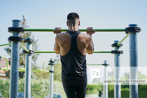 Rückenansicht eines Mannes  der an einem sonnigen Tag in einem Park Gymnastik macht