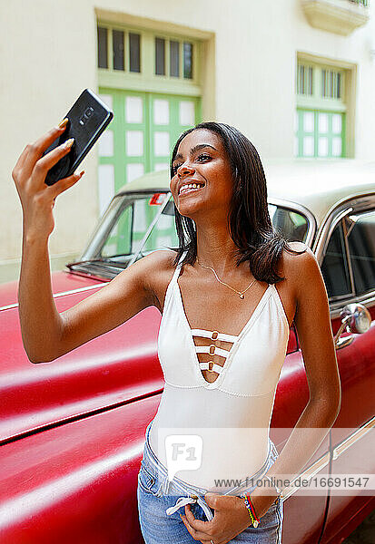 Junger Kubaner macht ein Selfie vor einem alten Auto in Havanna  Kuba