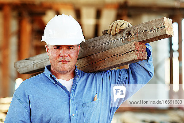 Männlicher Bauführer hält Holz und schaut in die Kamera