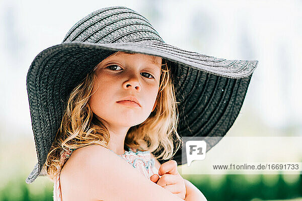 portrait of a sassy young girl staring at the camera with a sun hat on