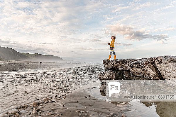 Pre-teen girl standing on rock at beach in New Zealand
